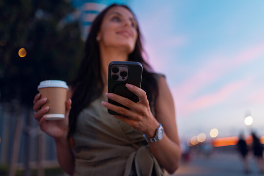 Woman holding smartphone and coffee at sunset
