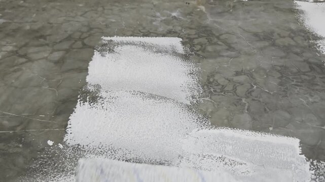 Point of view shot of a person using a paint roller on a long extension pole to apply white paint on a smooth dark concrete wall, ideal for DIY home improvement, renovation, and construction concepts.