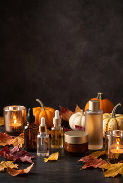 Autumn skincare products with pumpkins and candles on dark background