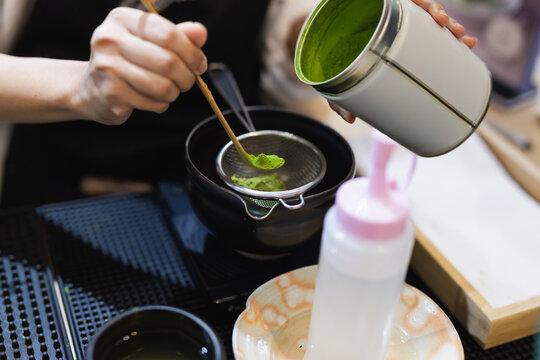 Barista sifting green matcha powder on strainer to prepare Japanese green tea.