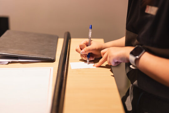 Hotel receptionist writing a notes on a small slip of paper at the wooden desk.