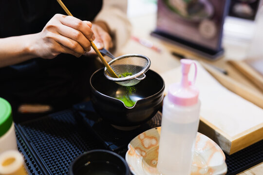 Barista sifting green matcha powder on strainer to prepare Japanese green tea.