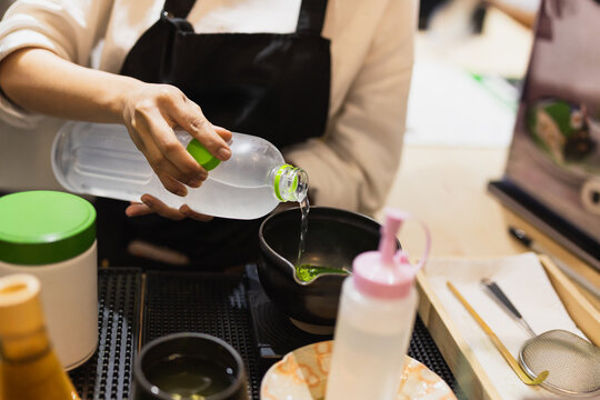 Barista pouring coconut juice from a bottle to prepare matcha green tea in a cafe.