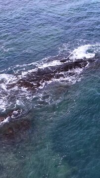 Aerial View of Ocean Waves Crashing Over Dark Coastal Rocks