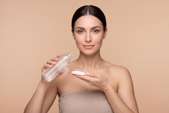 Beautiful young woman holding a bottle of micellar water and a cotton pad
