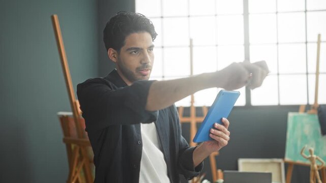 Man drawing on blue tablet with stylus, arm extended pointing while tapping screen in studio; creative focus.