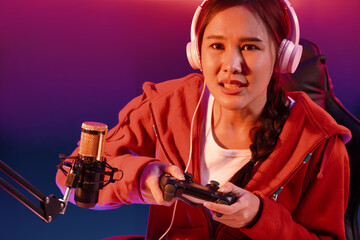 Host channel of beautiful Asian girl streamer with joystick playing online game wearing headphones pastel color talking with viewers media online. Esport skilled team players in neon room. Stratagem. © InfiniteFlow