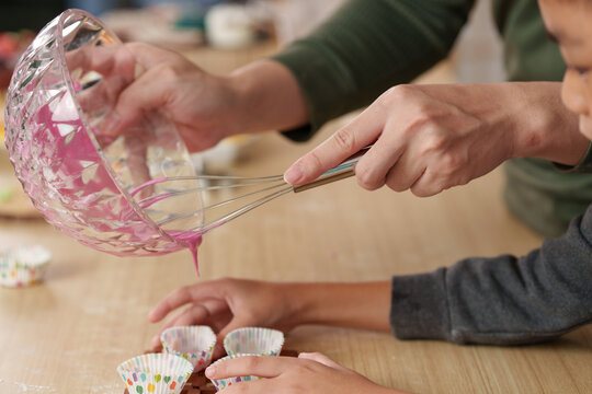 Cropped hands pouring pink batter into cupcake liners for home baking activity