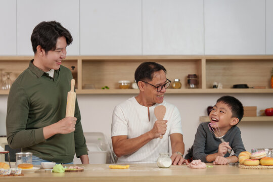 Three generations of Asian family singing with kitchen utensils while baking at home