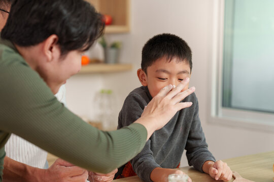 Asian father putting flour on son's nose during kitchen baking for family fun