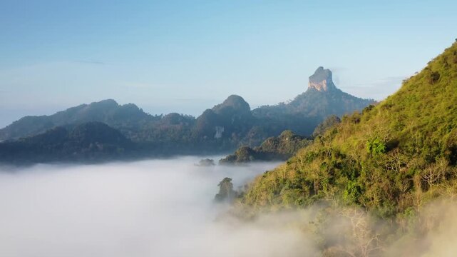 Unique karst landscape of KHAO SOK National Park, towering limestone mountains emerge from a thick blanket of morning fog, highlighting the lush tropical rainforest. Aerial view drone flight panorama