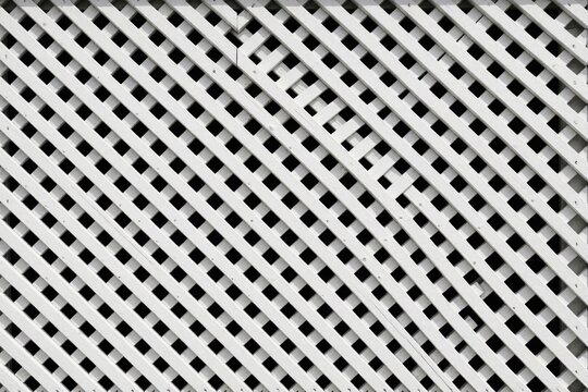 White wooden trellis lattice pattern with diagonal slats. Abstract geometric texture of crisscross timber fencing on wall. Minimalist background of white slats creates repetitive grid shape for
