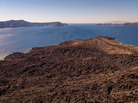 Drone aerial landscape of expansive black lava rocks on Nea Kameni island overlooking Santorini sea Greece