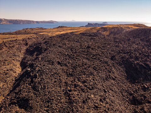 Drone aerial landscape of massive black volcanic lava slopes on Nea Kameni overlooking Santorini caldera Greece