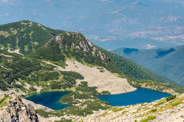 Fototapeta premium Deep blue, curved basin of the Georgiyski Lakes (Georgiyski Ezera) nestled below rugged granite slopes, scree fields, and pine-covered ridges, under a clear summer sky in Pirin National Park, Bulgaria