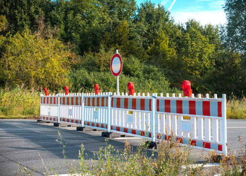 Asphalt road is blocked with a red and white plastic barriers due to construction work. Roadwork, no passage prohibited