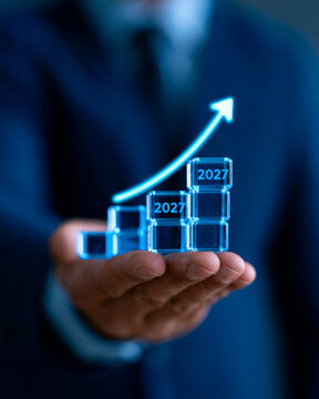 Business breakthrough and growth mindset drive expansion as professional hand presents futuristic graph with upward trend and years 2025 2026 2027 glowing in blue