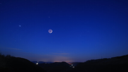 Blue hour time with crescent Moon, stars and planets above landscape silhouettes. © astrosystem