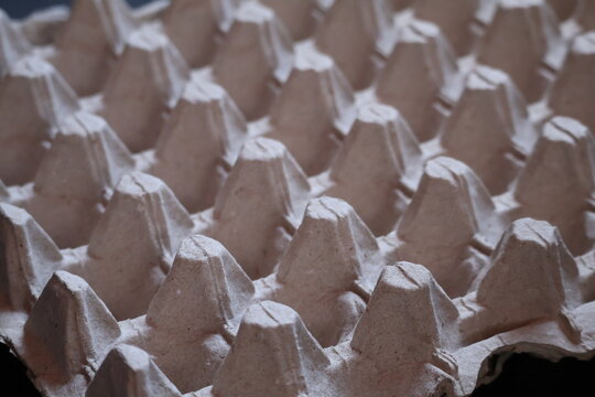 Closeup of pressed recycled cardboard egg tray texture, highlighting rough fibers, natural paper pulp, sustainable packaging, and earthy material details.