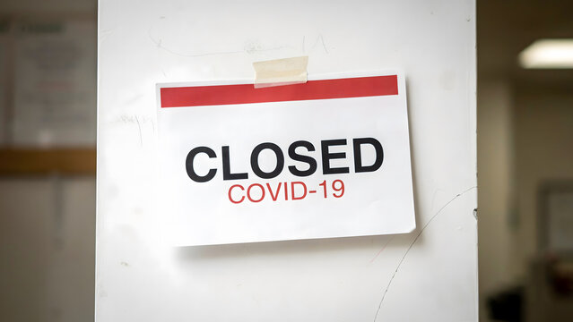 A white sign taped to a wall stating the business is closed due to covid 19