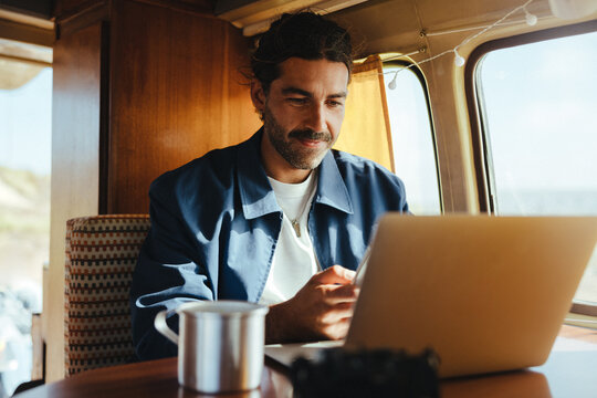 Working on the road: Man using laptop inside a camper van