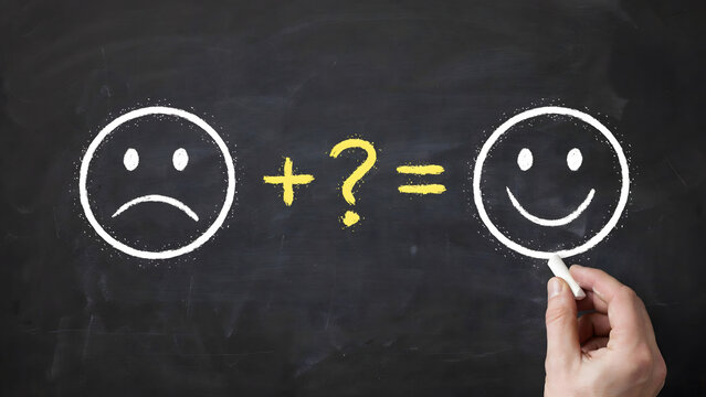 A hand drawing a happy face on a blackboard to transform sadness into joy