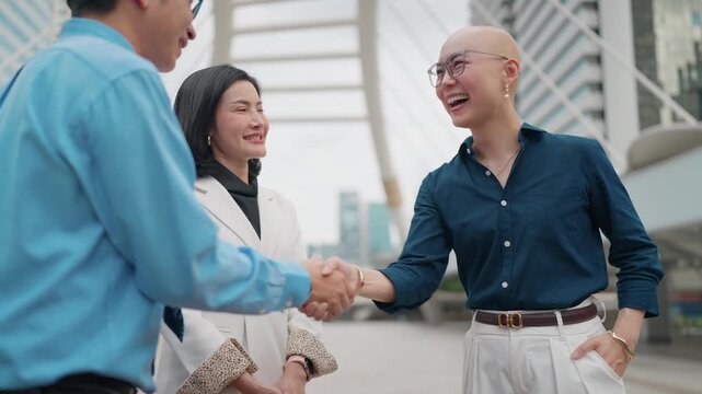 Business people shake hands outdoors near skyscrapers. They smile warmly, suggesting a successful agreement or greeting