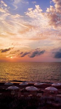 Vertical view of golden sunset over the sea horizon on an empty sandy beach with umbrellas