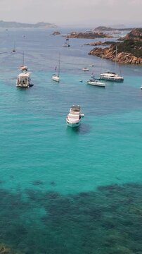 Aerial, vertical view of the turquoise bay with yachts and boats off the coast of Santa Maria Island in the La Maddalena archipelago, Sardinia, Italy