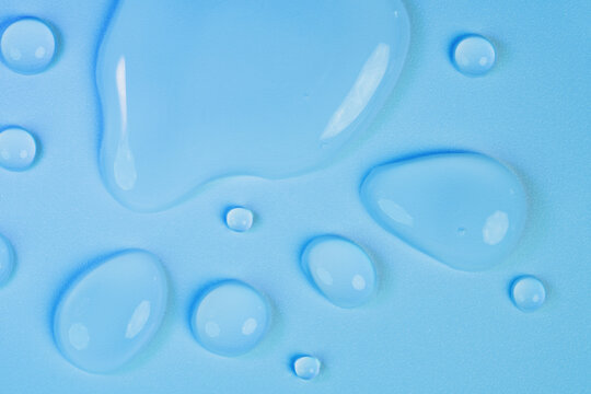 Macro shot of clear elongated water drops with light reflections on blue textured surface. Abstract wet background perfect for skin hydration, cosmetics, medical industries, purity, product backdrop.