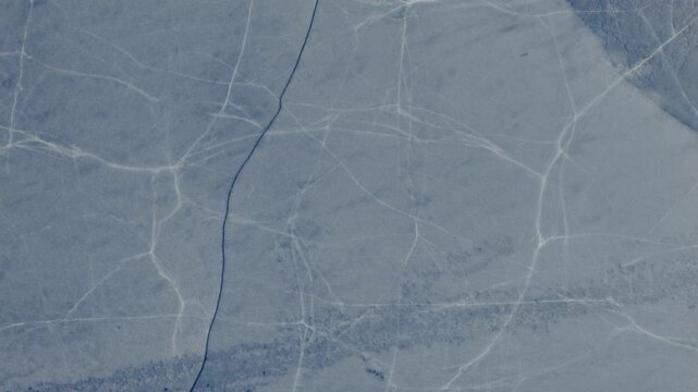 A top down aerial shot shows the icy patterns and snow-covered surface of a frozen lake in rural Norway