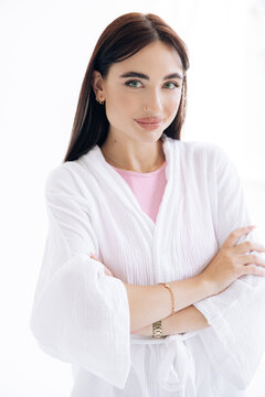 Female cosmetologist in white uniform standing with arms crossed.