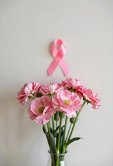 Naklejka premium Breast cancer awareness and support, pink ribbon with fresh flowers in a vase on a light background