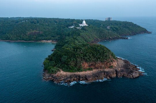 Spectacular aerial perspective of the forested Rumassala headland, featuring a white Japanese Peace Pagoda temple overlooking the vast deep blue ocean and scenic coastline.