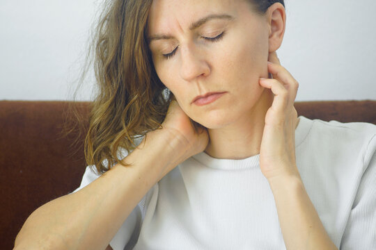 Close-up of woman massaging neck muscles with eyes closed to ease discomfort. Captures self-administered cervicogenic pain relief, headache massage technique, and somatic trigger point relaxation.