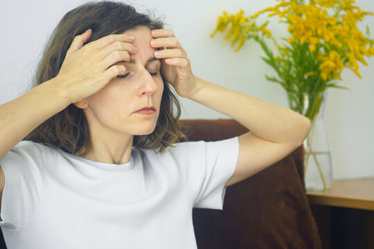 Woman pressing fingertips against forehead with eyes shut during self-acupressure session. Conveys facial tension relief technique, sinus headache management, and alternative holistic healing routine.