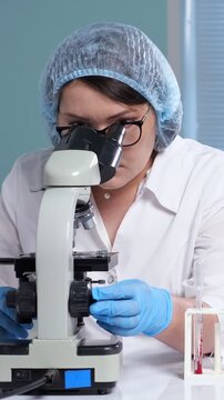 Professional female scientist performing microscopic analysis of a blood sample in a modern research laboratory, focusing on hematology and clinical diagnostics for disease study