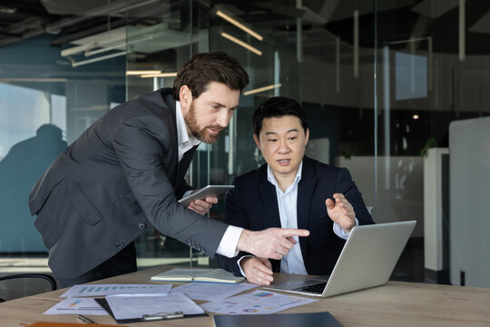 Two diverse business partners collaborating on a new project, working together and analyzing data on a laptop in a modern office meeting, discussing market trends and financial goals
