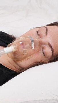Female patient with a serious illness receiving oxygen therapy through a mask while lying unconscious in a hospital bed, concept of critical medical care and respiratory distress