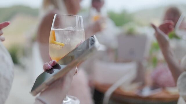 Woman holding smartphone and aperol spritz at party