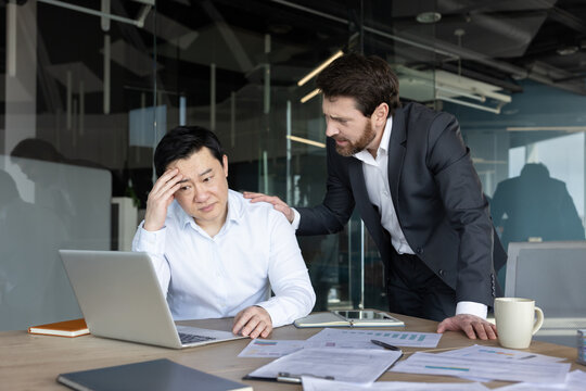 Business executive comforting a stressed asian colleague experiencing burnout and emotional failure at his office desk, showing empathy and support during a challenging work situation