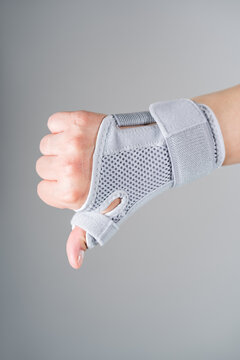 Thumb pain and carpal tunnel syndrome, joint pain and sprain. Close up of arm wearing orthopedic brace. Gray wrist splint with velcro straps