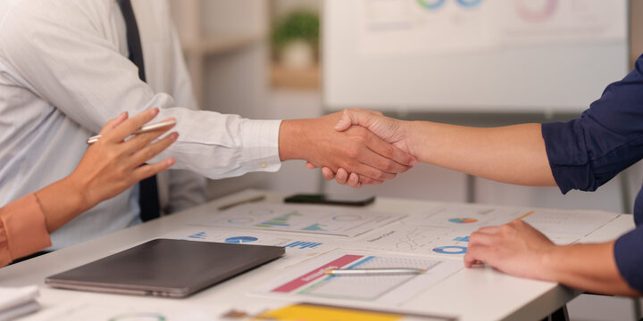 Business professionals shaking hands across table after corporate deal meeting