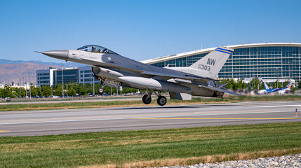 Fototapeta premium F16 fighter jet taking off from a military runway, landing gear just leaving the ground, powerful engine exhaust distortion, airport buildings in the background, dramatic low angle view, ultra photo