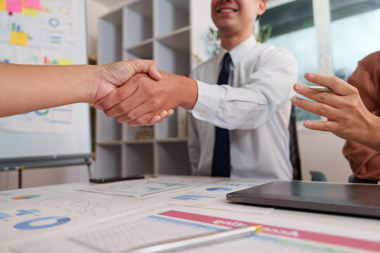 Business partners shaking hands over financial documents in office meeting for agreement