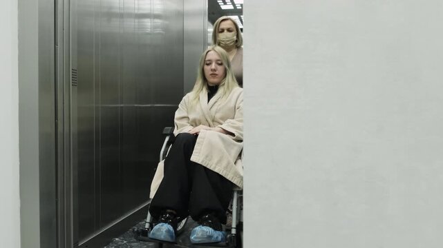 Nurse pushes wheelchair from modern elevator into medical corridor. Physician guides patient toward ultrasound examination room. Slow motion