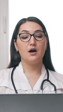Professional female doctor wearing a white coat and stethoscope using a laptop for an online consultation, providing remote medical advice and telehealth services to a patient from her office