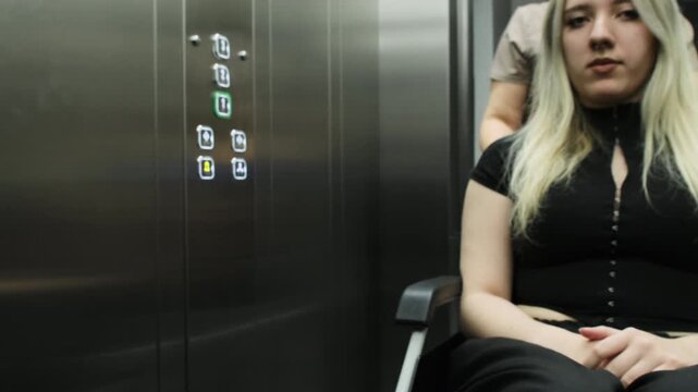 Physician wheels woman in wheelchair out of elevator into corridor of private clinic. Nurse rolls wheelchair through open elevator doors. Slow motion