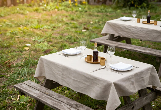 Outdoor dining and picnic setup, rustic garden party with table settings and wine bottle on wooden benches