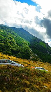 Parked car on mountain slope in Carpathian mountains, Romania. Transfagarash road. Automobile, green vegetation, hillside and dramatic cloud formation. Vertical video.
